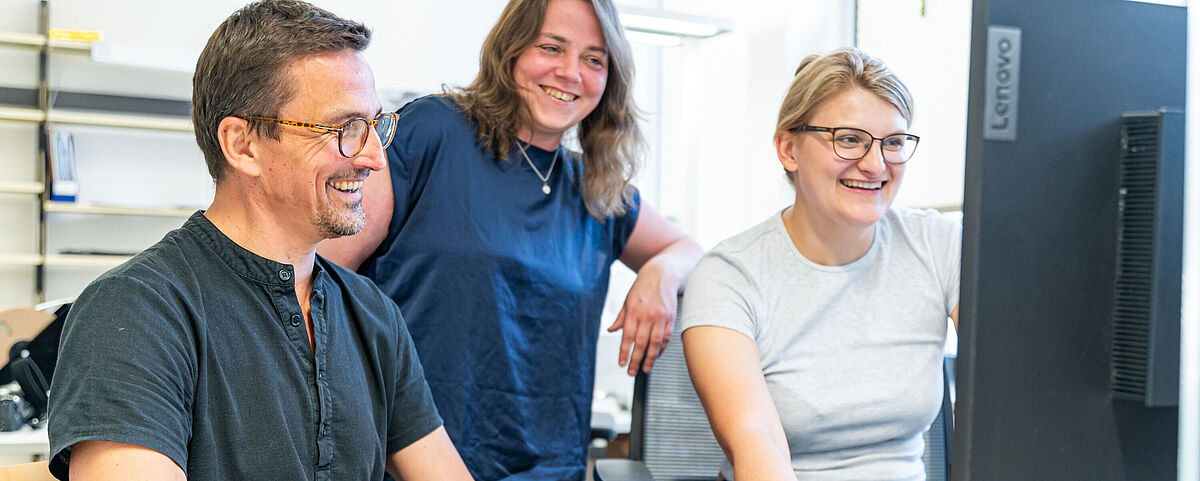 Arbeitgebermarketing Bibliotheken Ein Mann und zwei Frauen schauen lächelnd gemeinsam auf einen PC-Bildschrim.