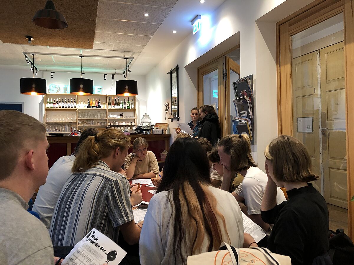 Outgoer Stammtisch Mehrere Personen sitzen in einem Restaurant rund um einen Tisch und unterhalten sich. Im Hintergrund ist die Bar zu sehen.