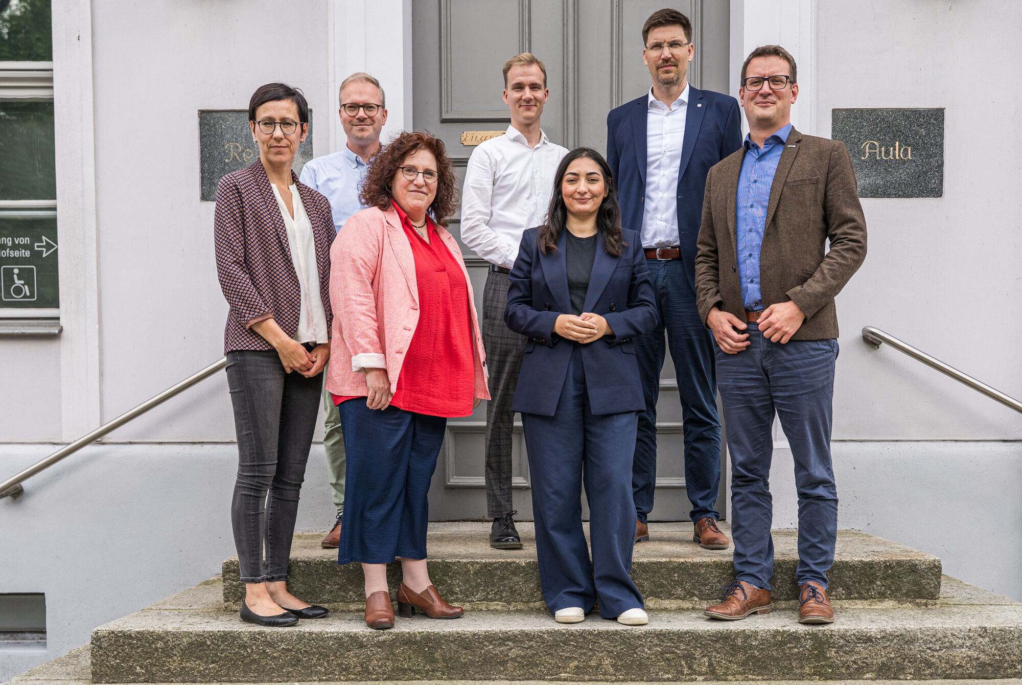 Gruppenbild mit der Bundesministerin für wirtschaftliche Zusammenarbeit und Entwicklung, Reem Alabali Radovan. Gruppenbild auf der Treppe vor dem Hauptgebäude der Universität mit der Ministerin (v.l.n.r. Dr. Juliane Huwe, Dr. Rick Tazelaar, Prof. Dr. Katharina Riedel, Lukas Voigt, Reem Alabali Radovan, Prof. Dr. Peter Michalik, Thomas Jenssen)