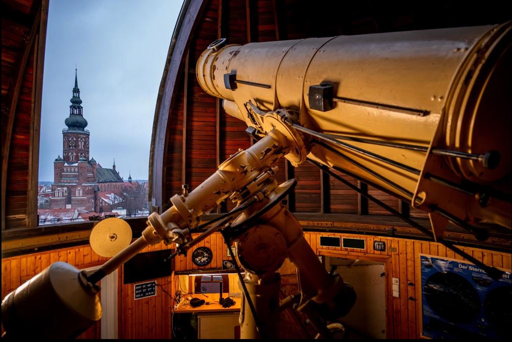 Blick aus dem Inneren der Sternwarte. Drinnen ein Teleskop. Draußen der Greifswalder Dom.