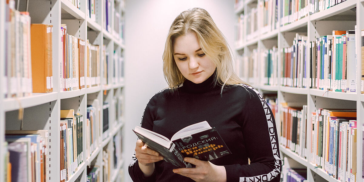 Symbolbild Studieren und Lernen in der Bibliothek Auf dem Foto sieht man eine junge Studentin, welche ein Buch zur russischen Sprache liest.