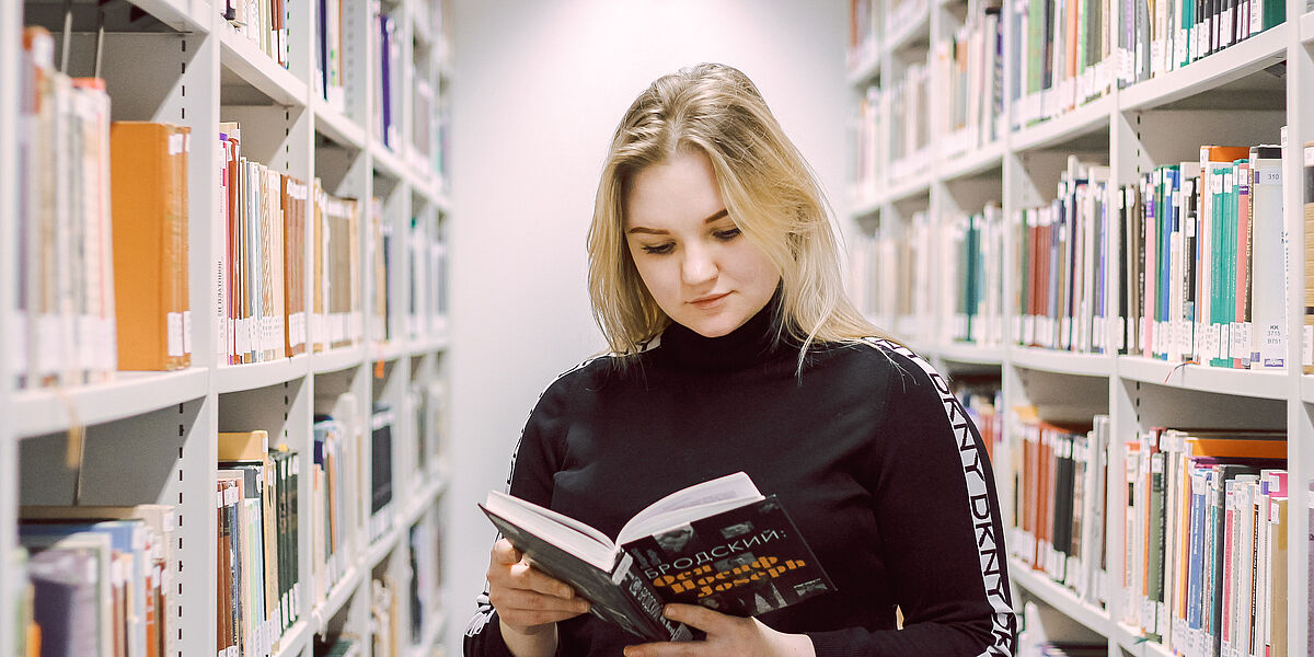 Symbolbild Studieren und Lernen in der Bibliothek Auf dem Foto sieht man eine junge Studentin, welche ein Buch zur russischen Sprache liest.