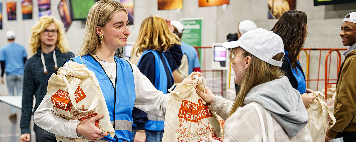 Ersti-Begrüßung 2024 Eine Studentin steht mit einem Beutel in der Mensa und begrüßt Erstsemesterstudierende