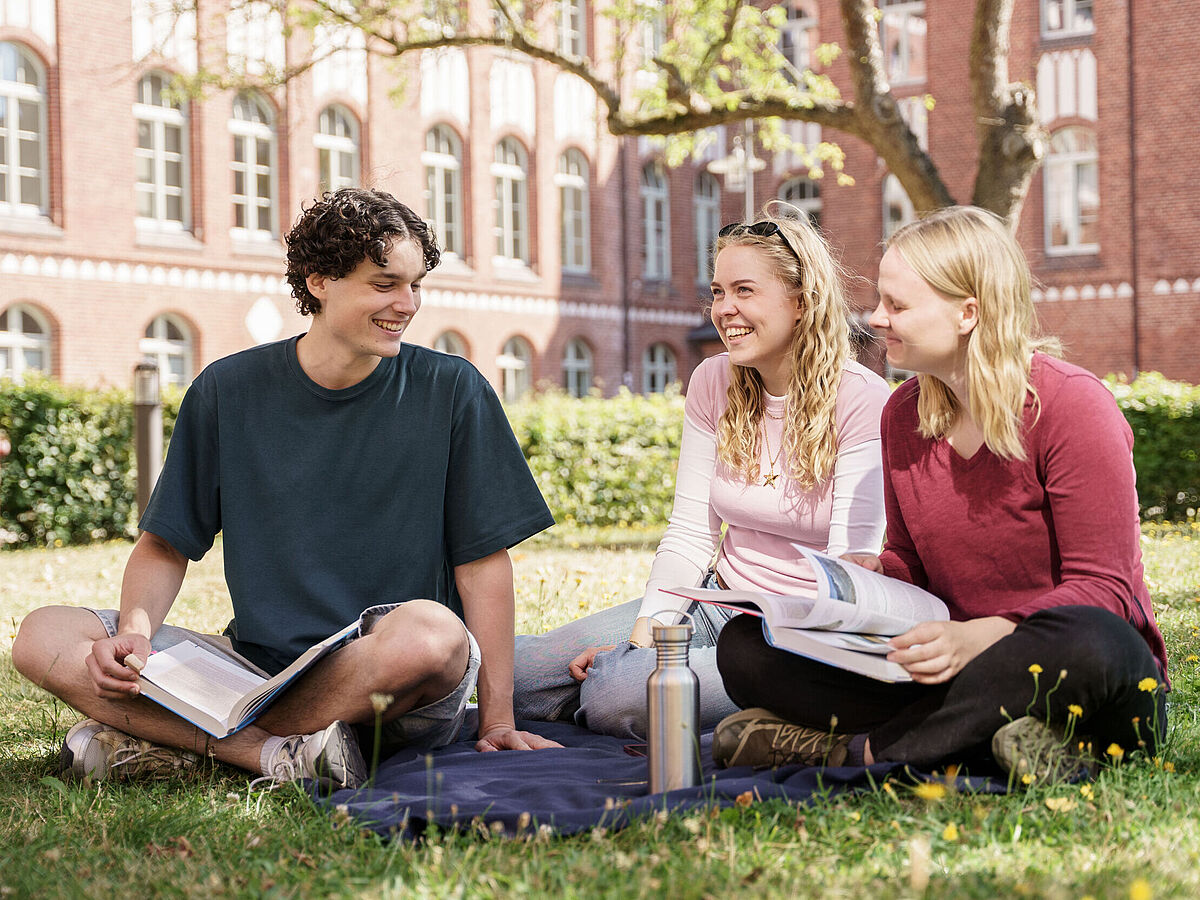 Studieren in Greifswald Studierende sitzen auf dem Rasen im Apfelgarten und unterhalten sich und lachen dabei.