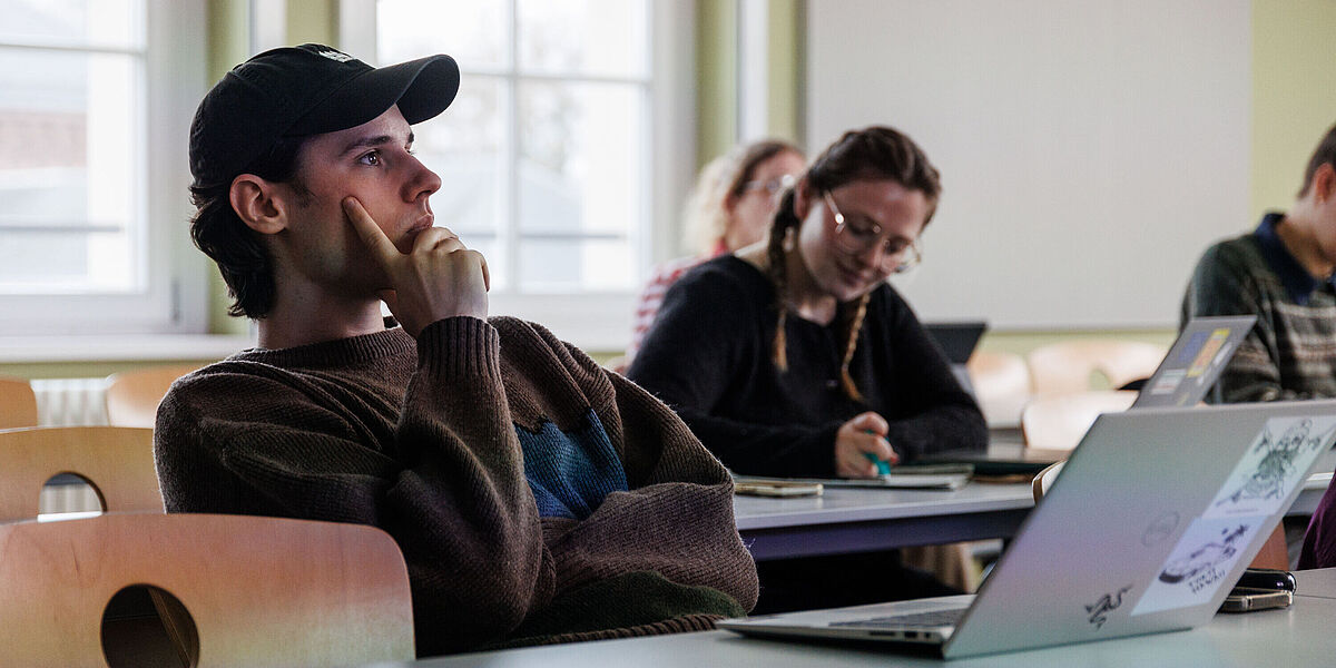 Symbolbild Philosophie Studierende im Seminarraum bei einem Philosophie-Seminar. Im Vordergrund sitzt ein Student, der ein Basecap trägt.