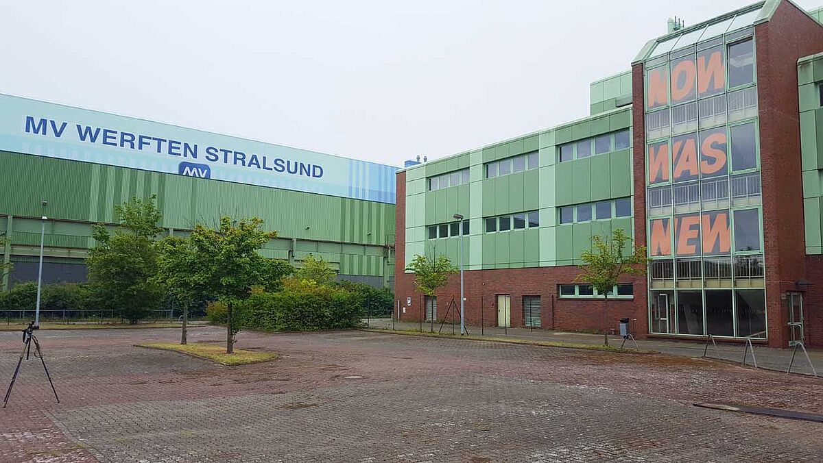 Man sieht das Gebäude der Werft, an dessen Fassade der Schriftzug "NOW WAS NEW" in roten, großen Buchstaben zu sehen ist. Eine Intsallation der Künstlerin Susanne Gabler.