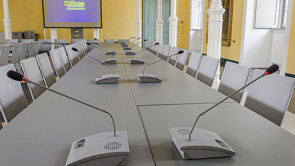 Es ist der Konferenzraum der Universität zu sehen. Auf den Tischen stehen Mikrofone einer Sprechanlage. ild Sitzungen mit Sprechanlage