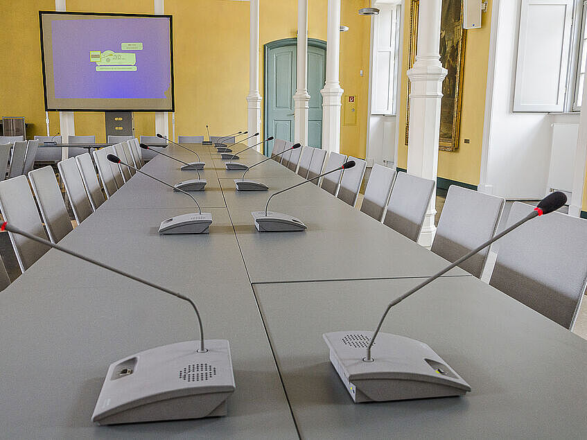 Es ist der Konferenzraum der Universität zu sehen. Auf den Tischen stehen Mikrofone einer Sprechanlage. ild Sitzungen mit Sprechanlage