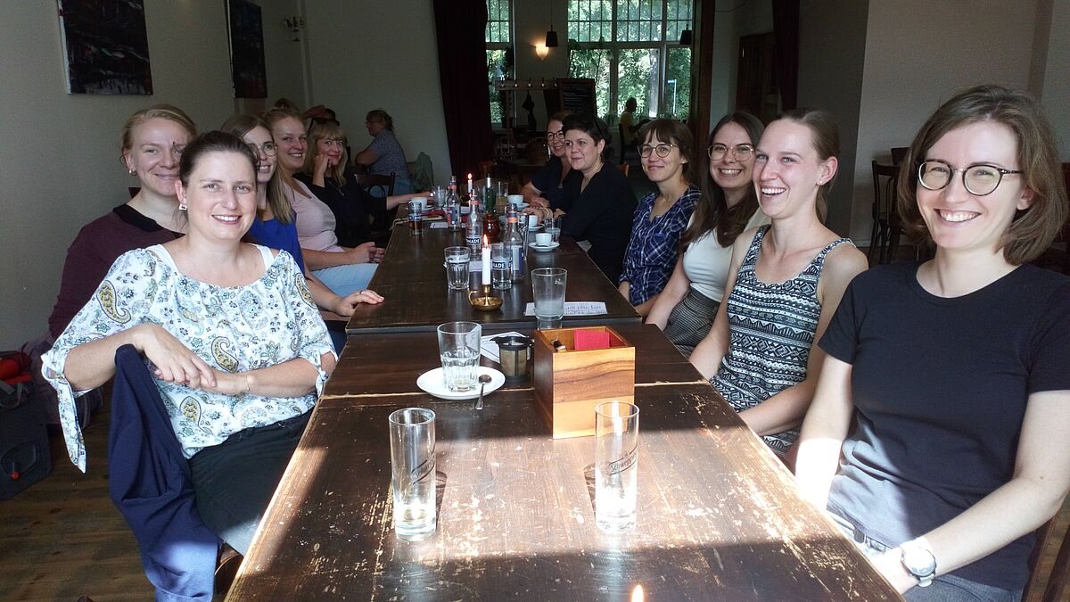 Mehrere Frauen sitzen an einem langen Tisch in einem Restaurant und lächeln in die Kamera