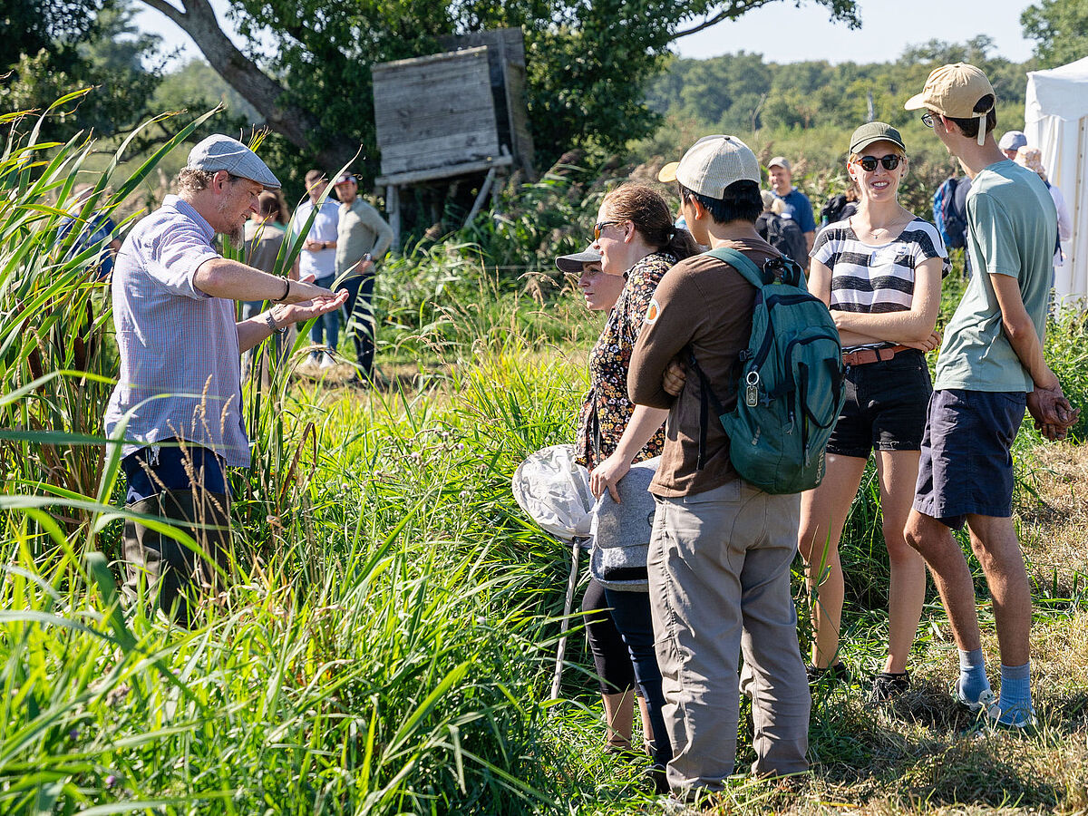 Symbolbild Moorforschung Mehrere Personen stehen in einer Moorlandschaft und hören dem Referenten zu.