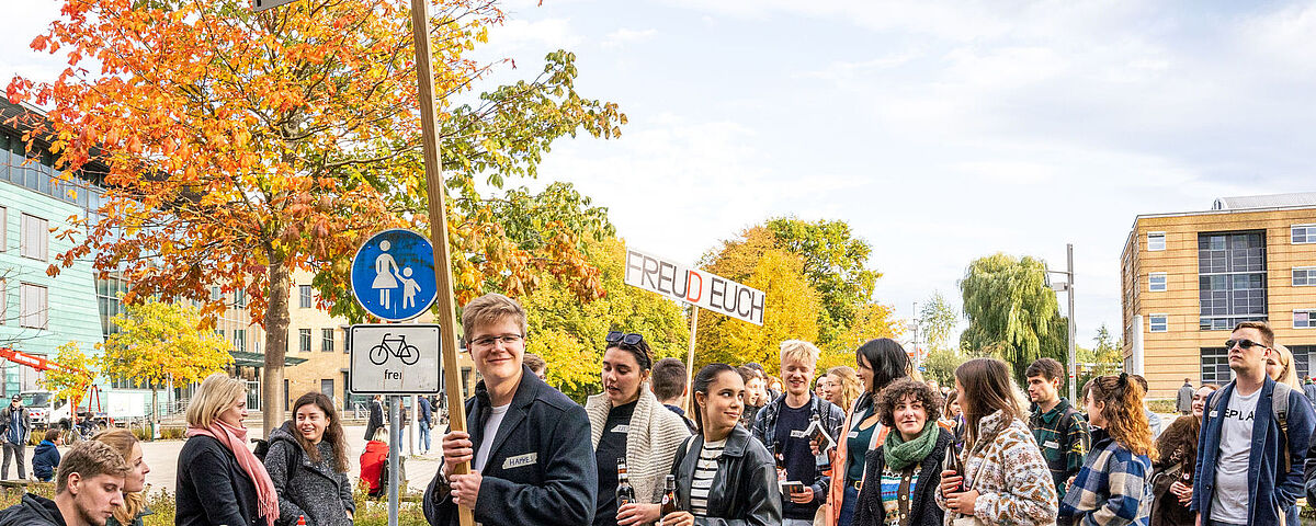 Ersti-Begrüßung Viele Studierende versammeln sich zur Ersti-Begrüßung auf dem Beitz-Platz. Es werden Banner hochgehalten zur Orientierung. Studierende unterhalten sich angeregt.