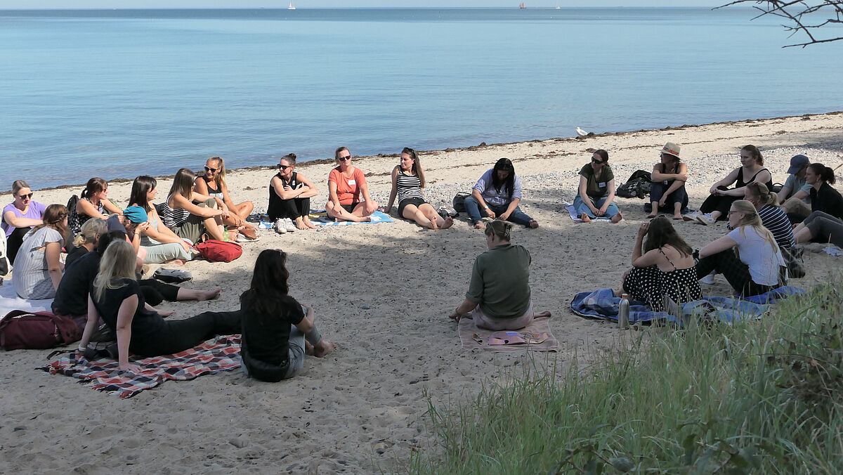 Eine Gruppe von Frauen sitzen am Strand im Kreis.