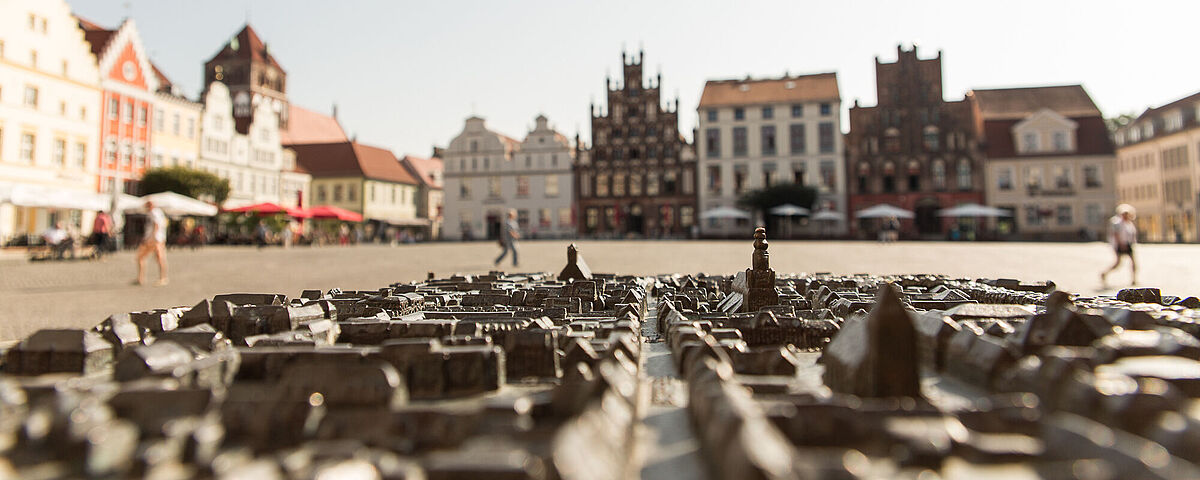 Heimathafen Marktplatz Im Vordergrund sieht man ein gusseisernes Modell der Stadt Greifswald und im Hintergrund die Gebäude des Marktplatzes.
