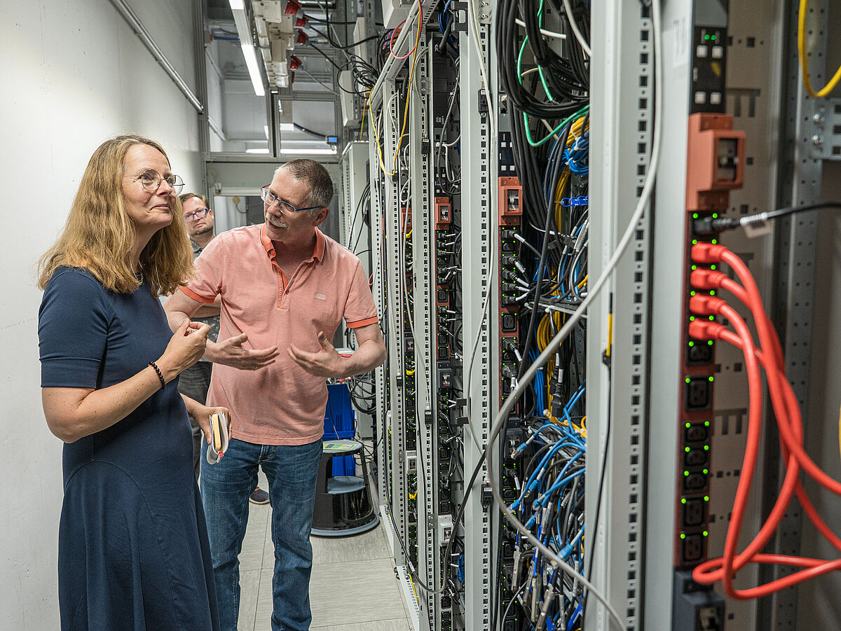 Bettina Martin (Wissenschaftsministerin MV) im Gespräch mit Prof. Dr. Ralf Schneider Eine Frau und ein mann stehen vor viel Technik im Rechenzentrum.