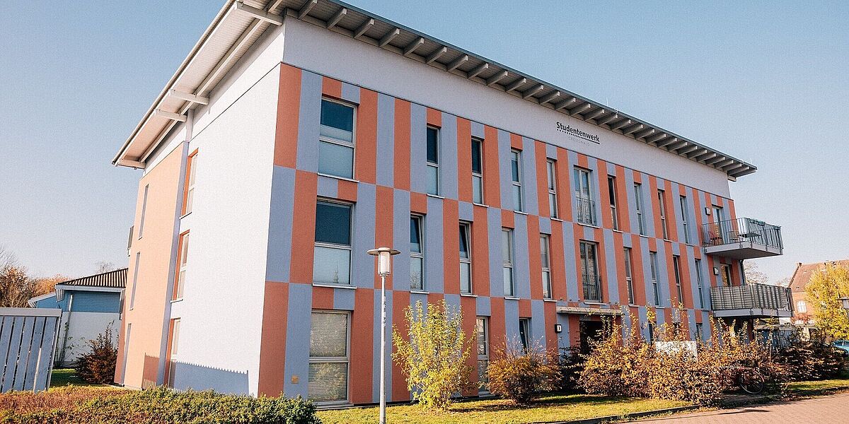 Wohnheim Studierendenwerk Von außen ist bei Sonnenschein und blauem Himmel das blau- und orangefarbene Wohnheim in der Fleischerwiese zu sehen