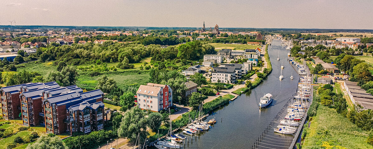 Greifswald von oben Luftaufnahme wie der Ryck sich durch die sommerliche Stadt schlängelt. Rechts und links am Ufer stehen Schiffe.