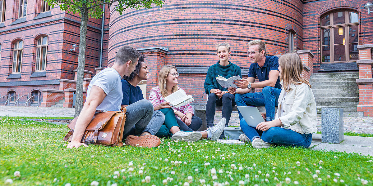 Studierende am Historischen Campus Eine Gruppe von Studierenden sitzt auf einer sommerlichen Wiese im Hinterhof des Historischen Campus mit Laptops und aufgeschlagenen Büchern.