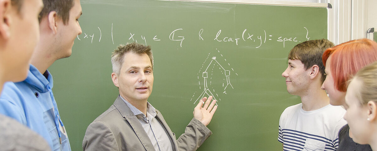 Symbolfoto Mathematik-Studium Mehrere Personen stehen vor einer Tafel, auf der mathematische Formeln abgebildet sind.