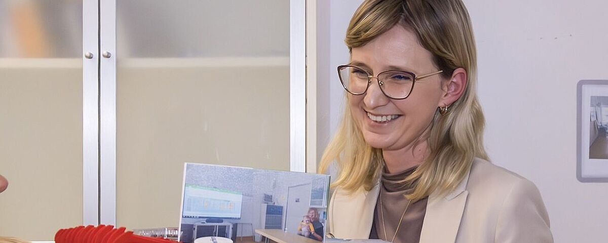 Linda Schönborn guckt glücklich auf ein Geschenk zur Habilitation (ein Hut, dekoriert mit wissenschafts-assoziierten Gegenständen)