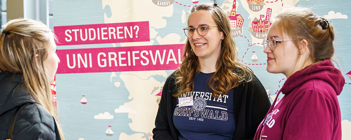 Symbolbild Hochschulinfotage Eine interessierte Personen lässt sich an einem Stand während der Hochschulinformationstage von zwei Studentinnen beraten.