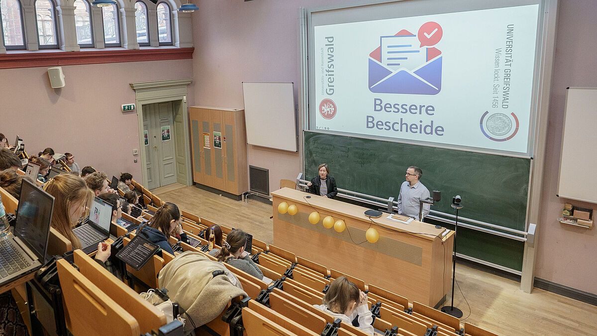 Projekt „Bessere Bescheide“ Mehrere Personen sitzen im Hörsaal und hören den Dozierenden zu.