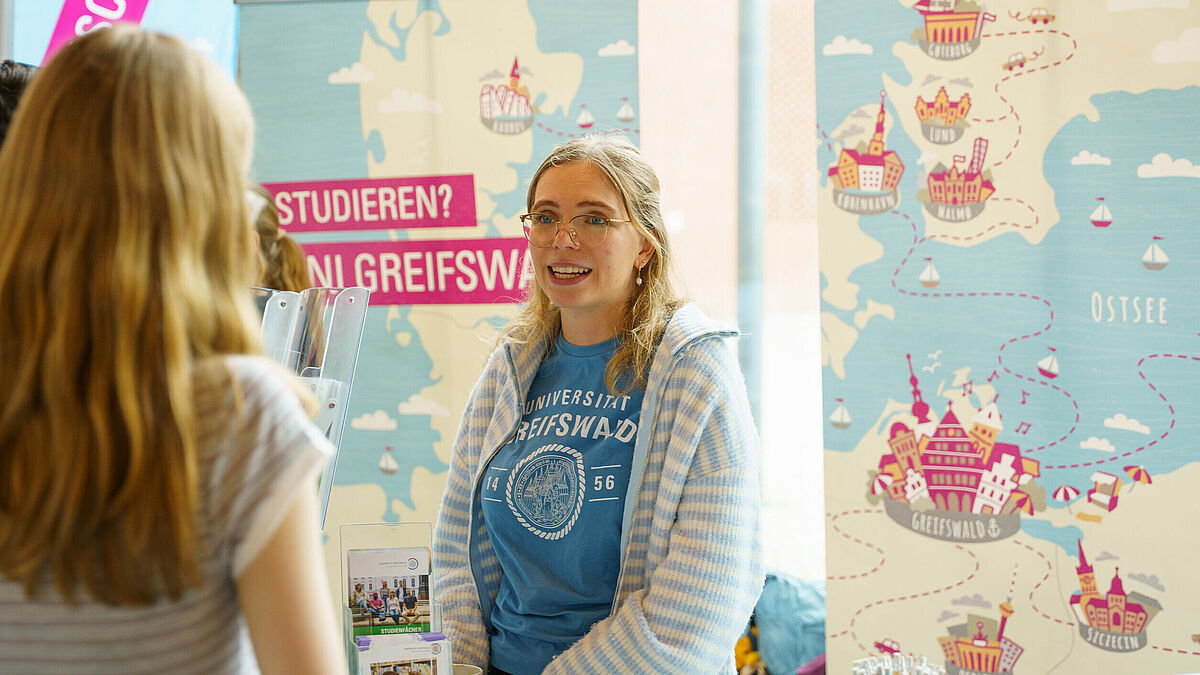 Hochschulinfotage Beratung Eine junge Frau unterhält sich mit Menschen und berät sie freundlich zum Studium.