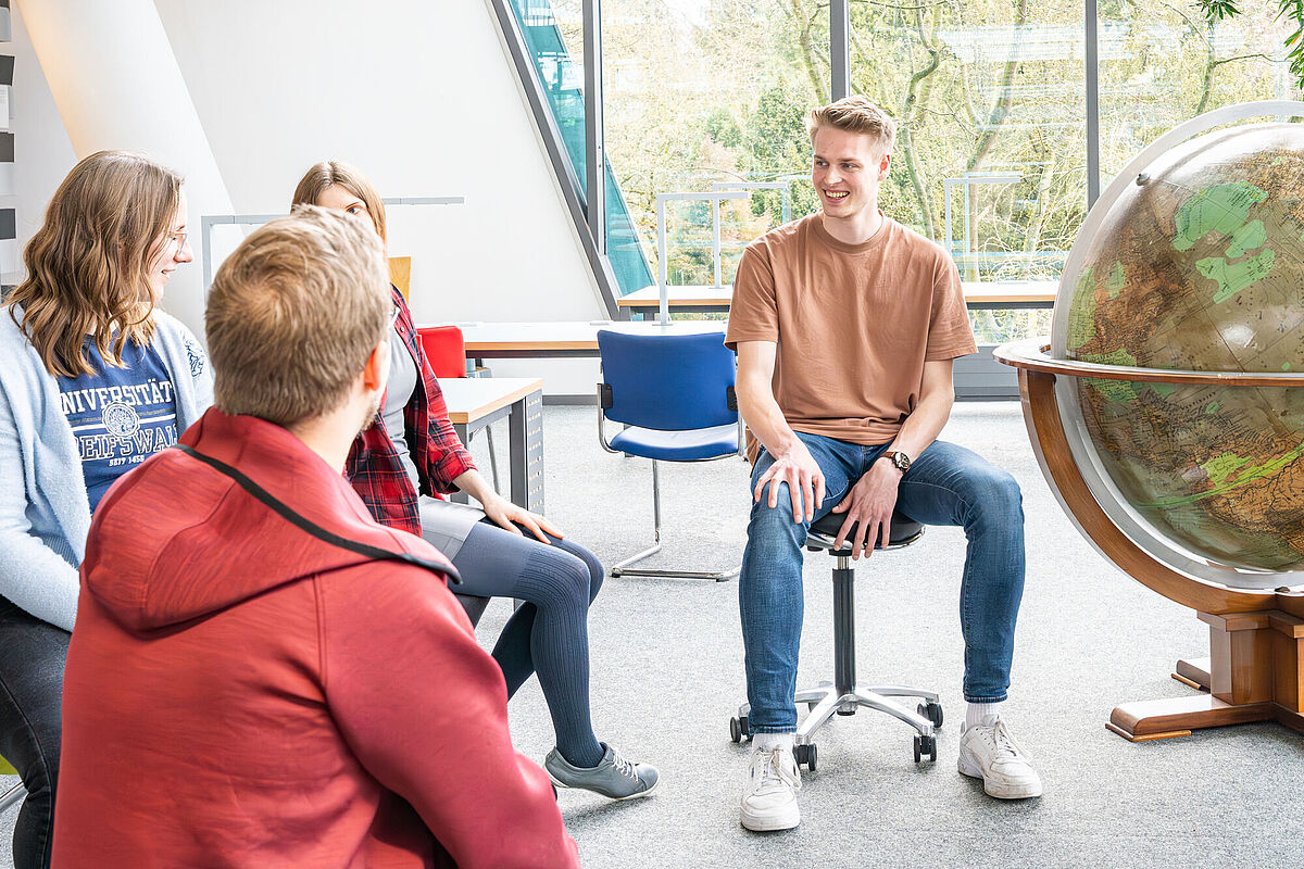 Gruppenarbeit / Projektarbeit In einem lichtdurchfluteten Raum sitzt eine Gruppe junger Menschen und diskutiert über ein Thema.