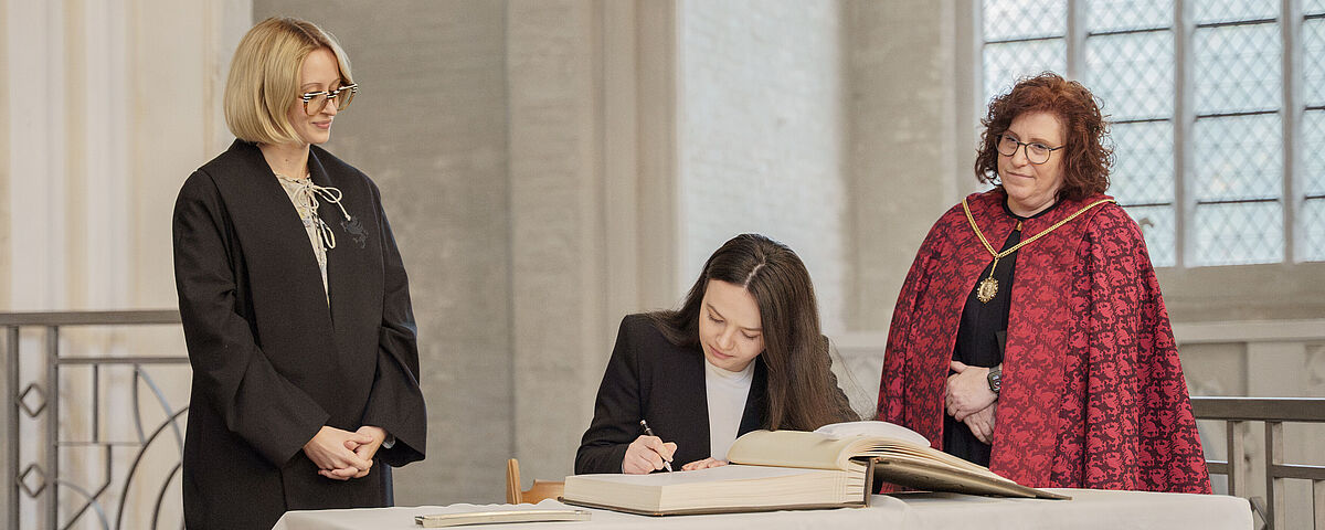 Einschreibung in das Ehrenbuch der Universität Eine junge Frau schreibt sich in ein alten großes Buch in einer alten Kirche ein.